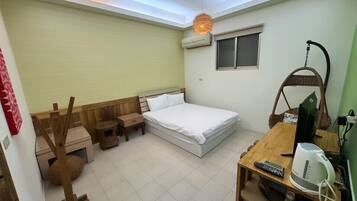 Habitación compacta con una cama individual, una mesita con hervidor, una silla y una lámpara colgante.