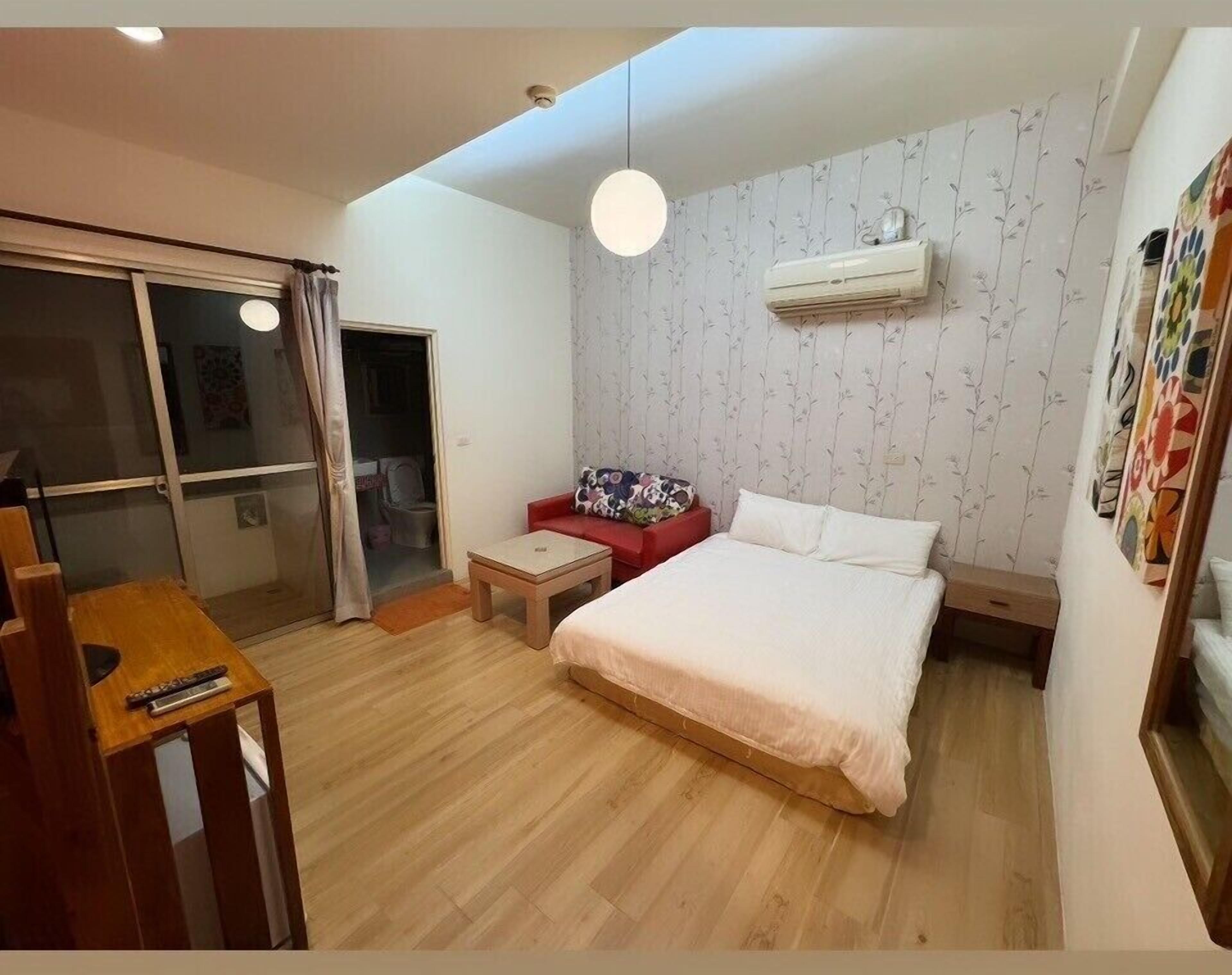 A bedroom with a bed, a red sofa, a small table, and a ceiling light.