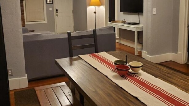 Un comedor con una mesa de madera, bancos, una lámpara y un televisor.