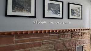 Tres fotografías en blanco y negro enmarcadas en una pared, con el texto "WELCOME TO LAVA COTTAGE" debajo.