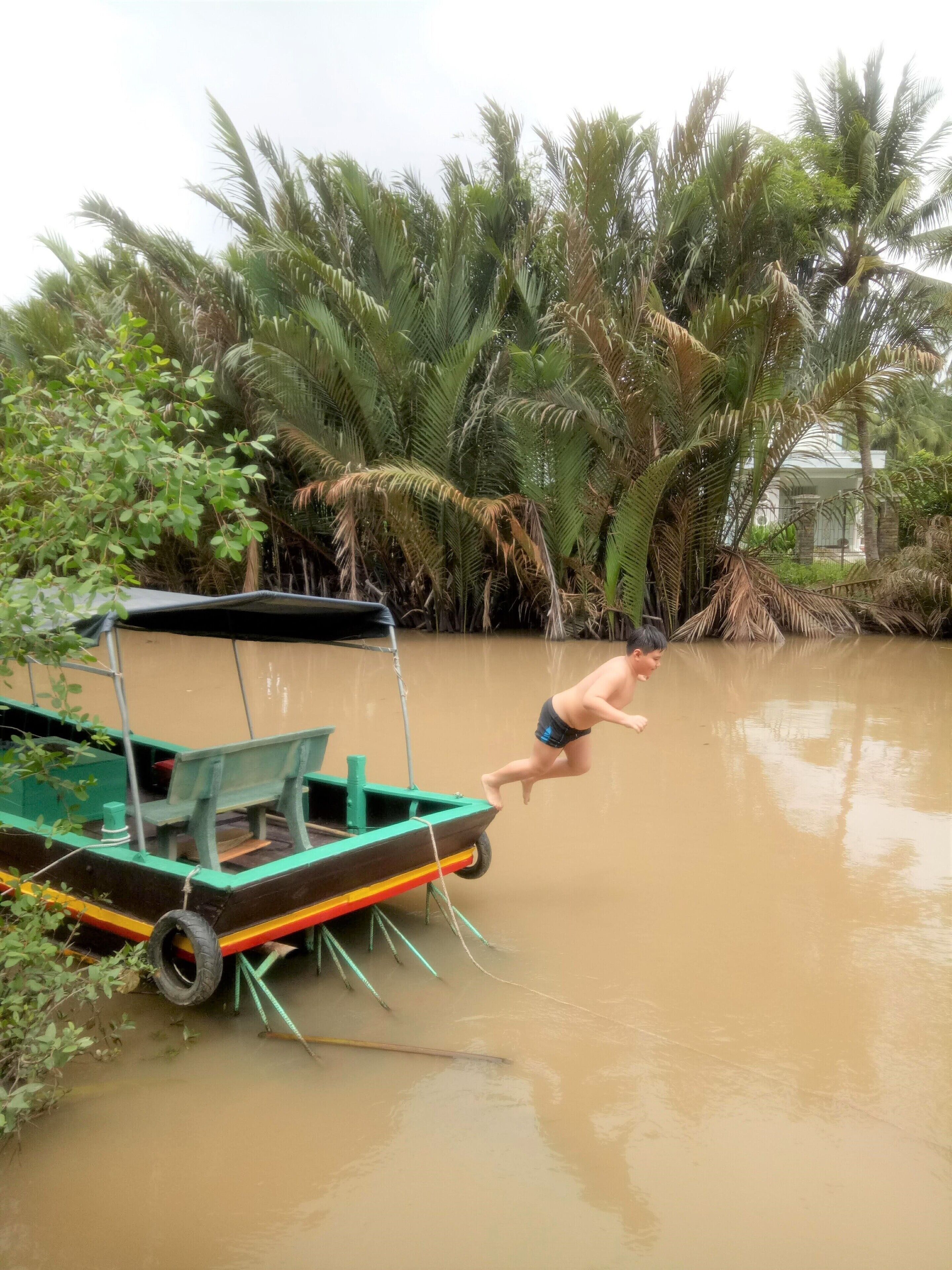 A man jumping from a boat into a muddy water body surrounded by dense vegetation.
