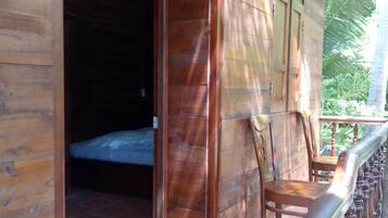Una cabaña de madera con balcón, una cama a la vista en su interior y suelo de baldosas.