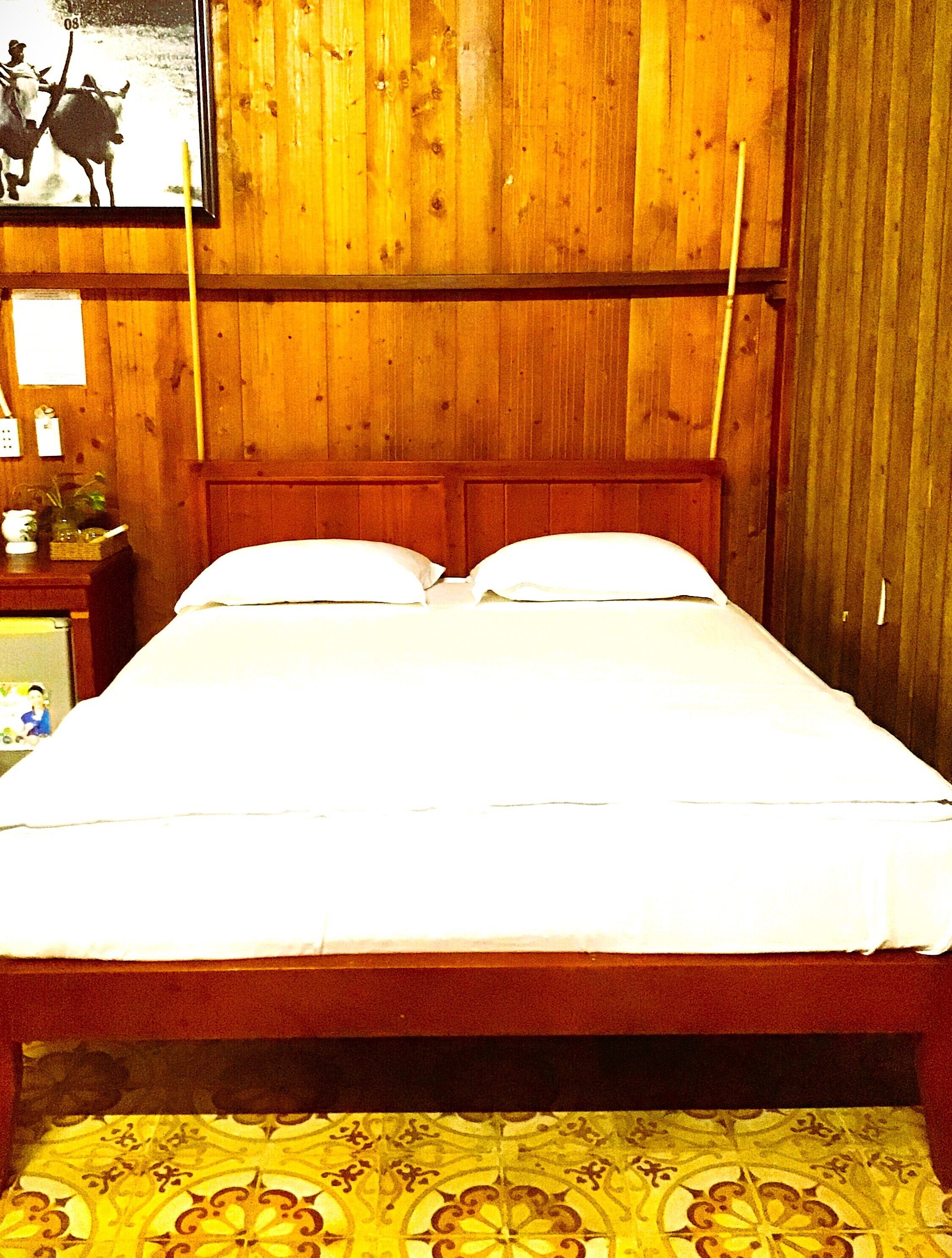 Een houten bed met witte lakens in een kamer met houten lambrisering.