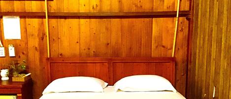 Een houten bed met witte lakens in een kamer met houten lambrisering.