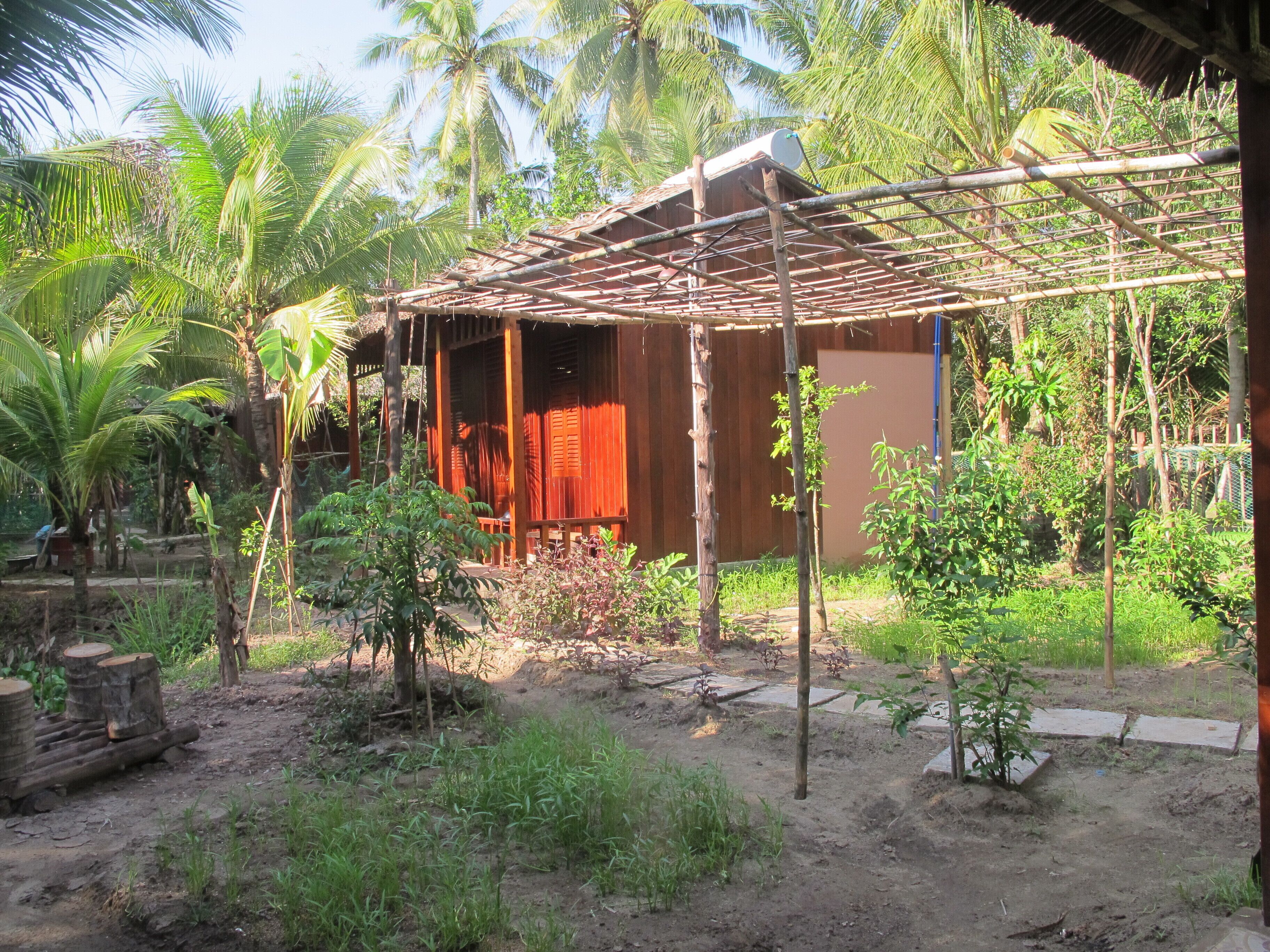 A rustic wooden structure with a thatched roof, surrounded by lush greenery and palm trees.