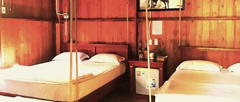 A room with two beds, wooden walls, a small table with a lamp, and a picture on the wall.