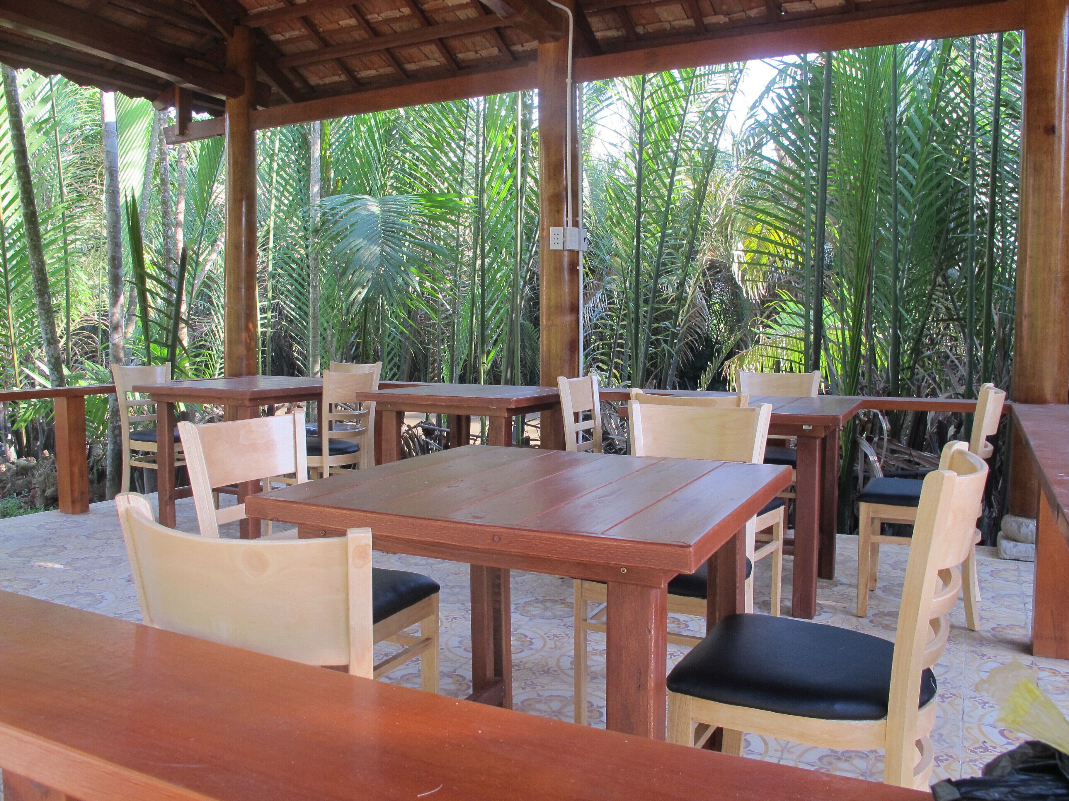 An outdoor wooden pavilion with tables and chairs, surrounded by lush tropical vegetation.