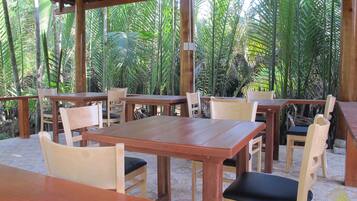 An outdoor wooden pavilion with tables and chairs, surrounded by lush tropical vegetation.