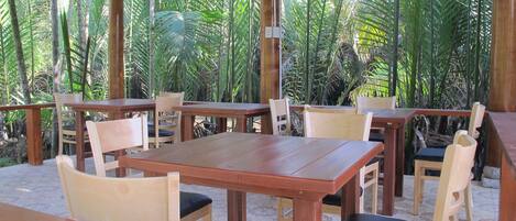 An outdoor wooden pavilion with tables and chairs, surrounded by lush tropical vegetation.