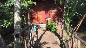 A narrow pathway leading to a red building with a wooden fence on either side, surrounded by lush greenery.