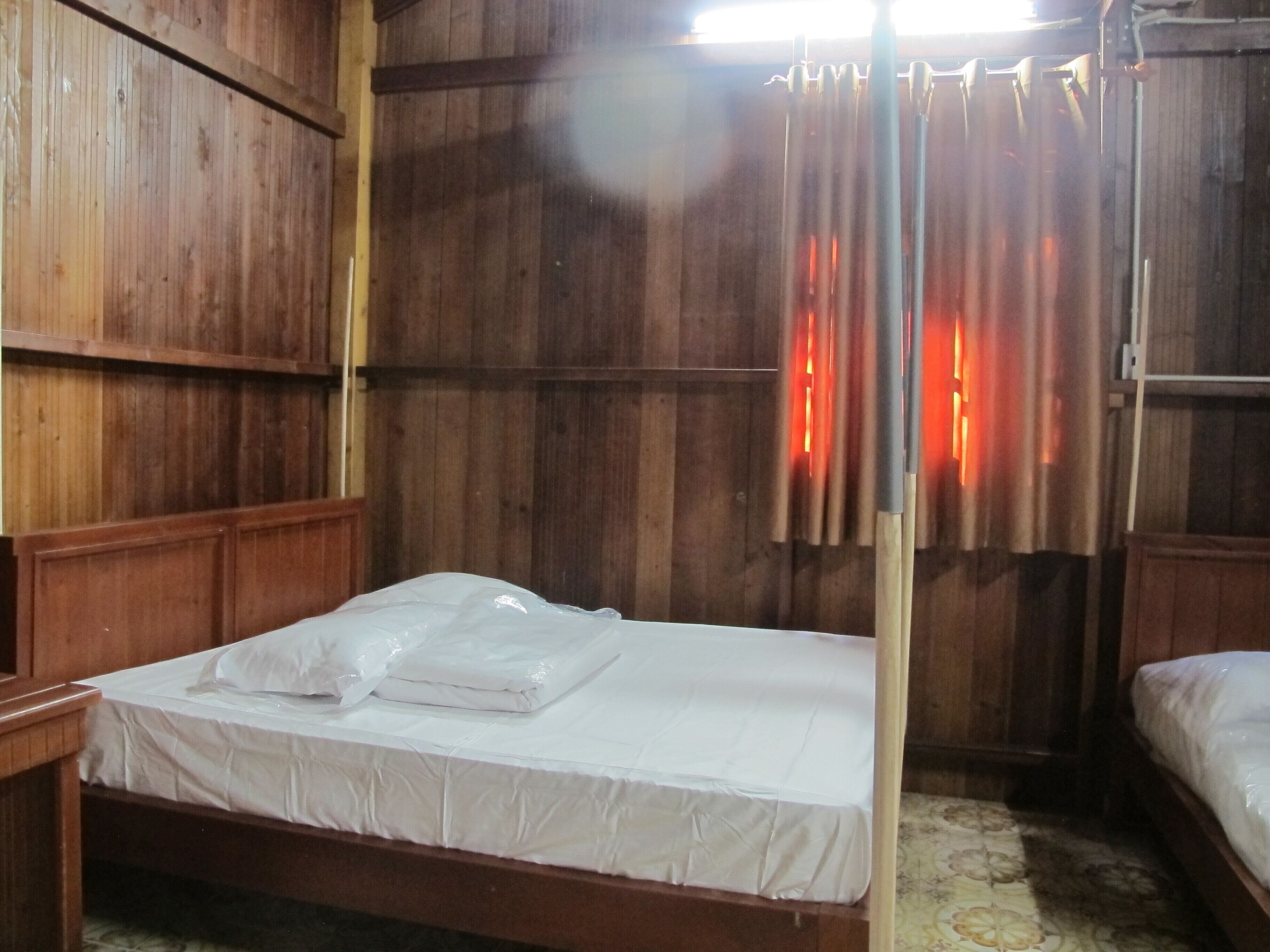 A wooden room with a single bed, wooden walls, and a curtain.