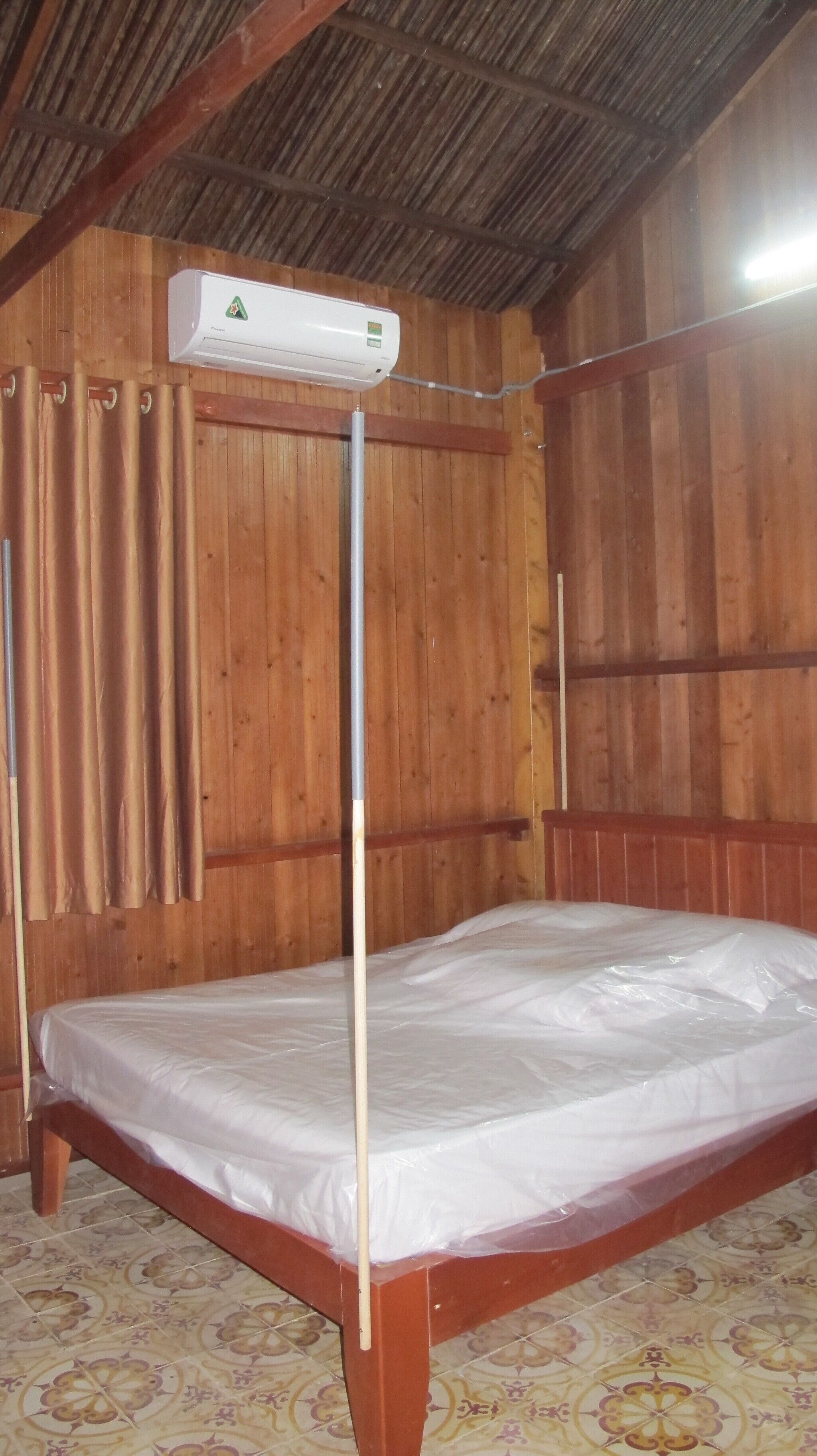 Ein Einzelbett aus Holz mit einer Matratze und einem Metallgestell in einem Raum mit Holzwänden und einer schrägen Decke.