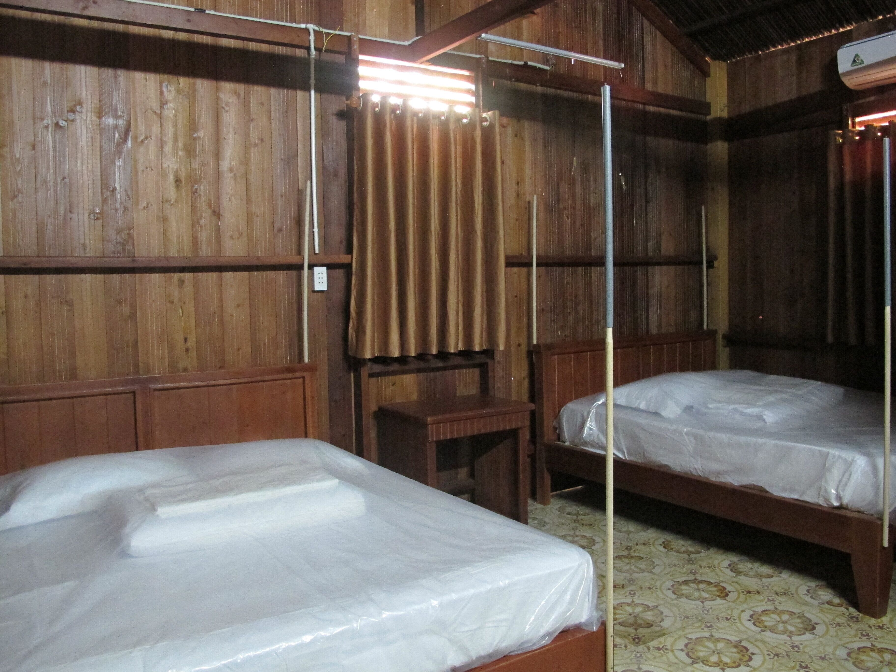 Una habitación de madera con dos camas, una mesita y una cortina.