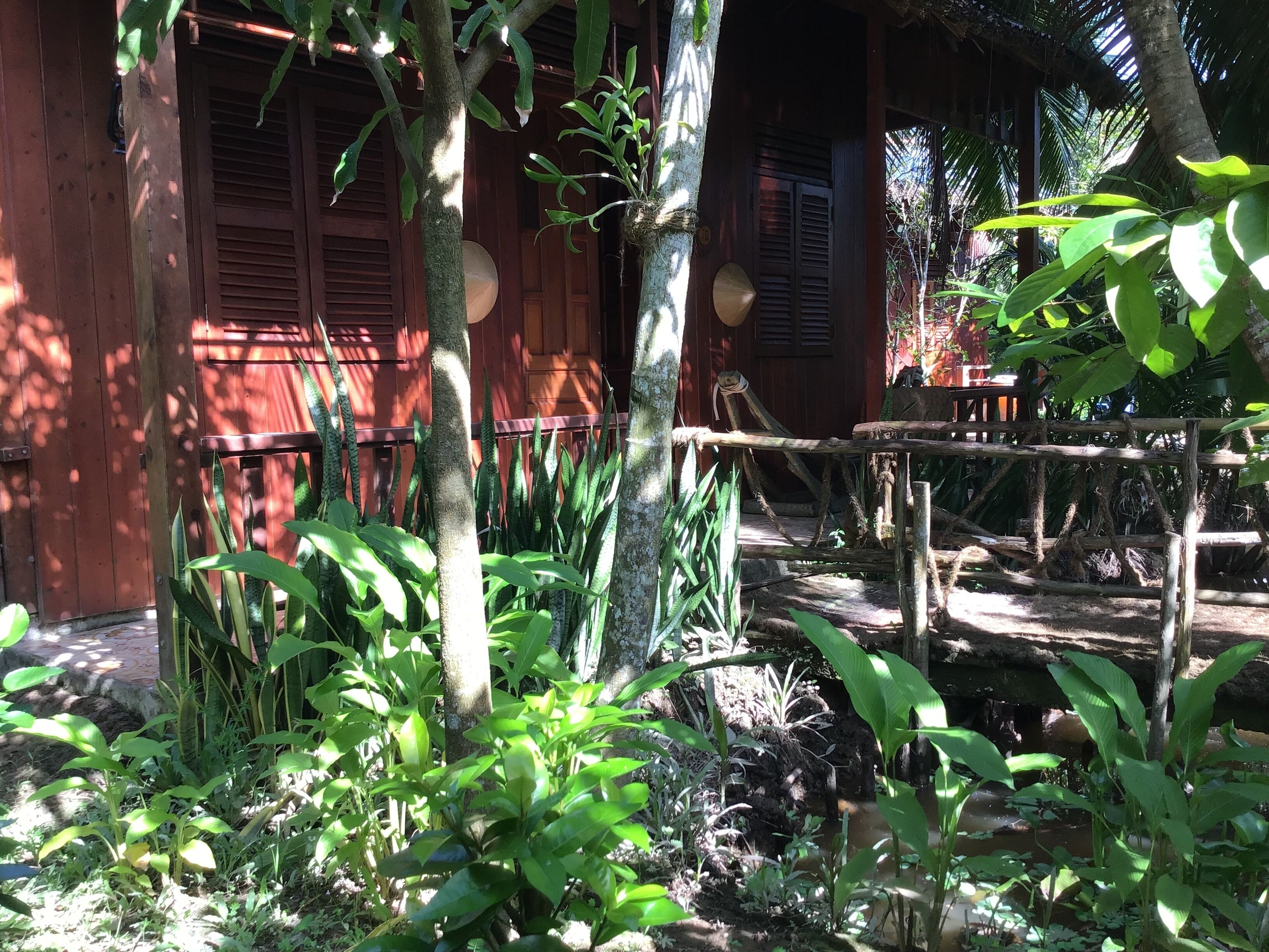 A rustic wooden building with a thatched roof, surrounded by lush greenery and a wooden fence.