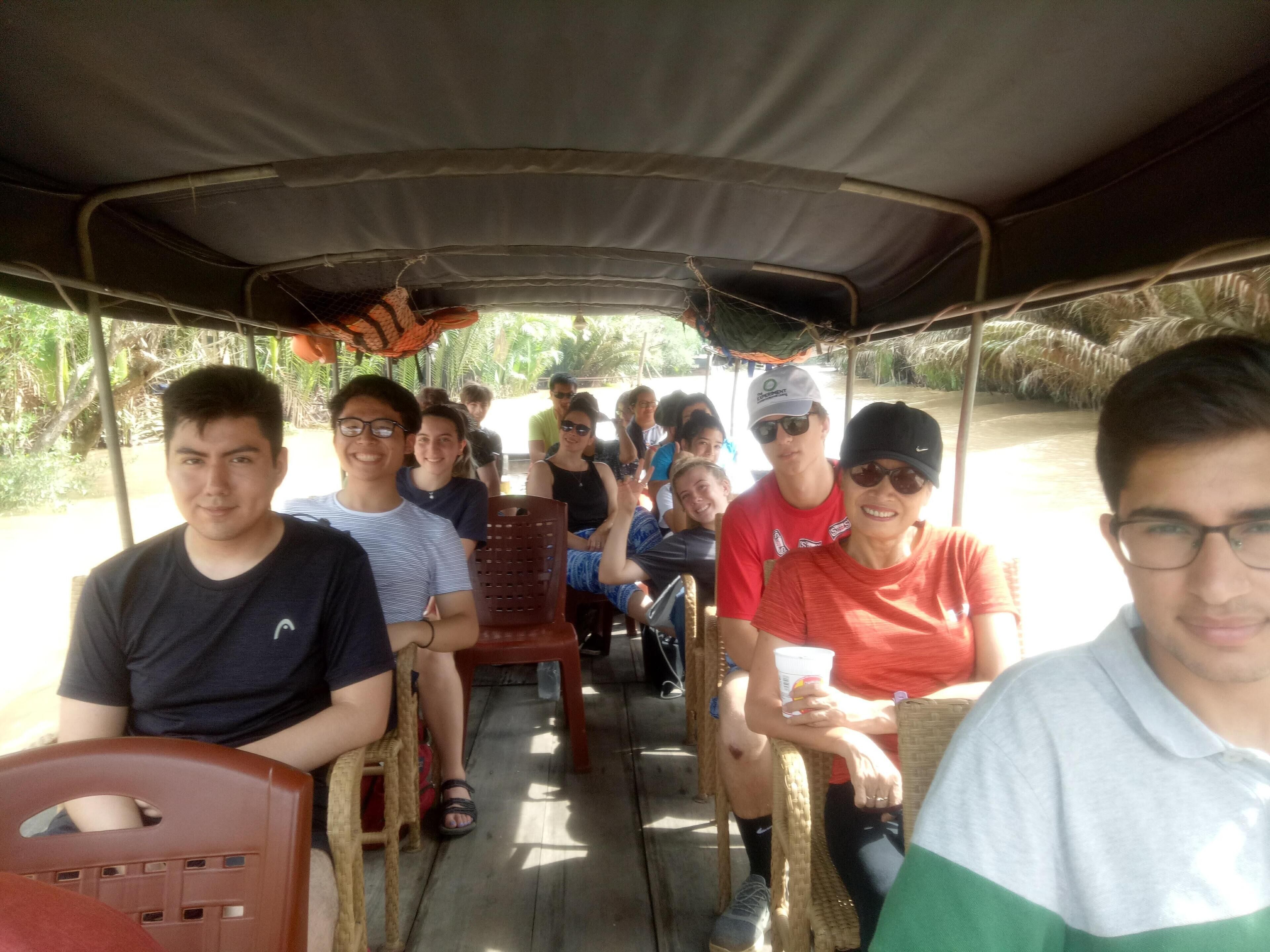 A group of people seated inside a covered vehicle with a thatched roof, likely a tour or transport vehicle.
