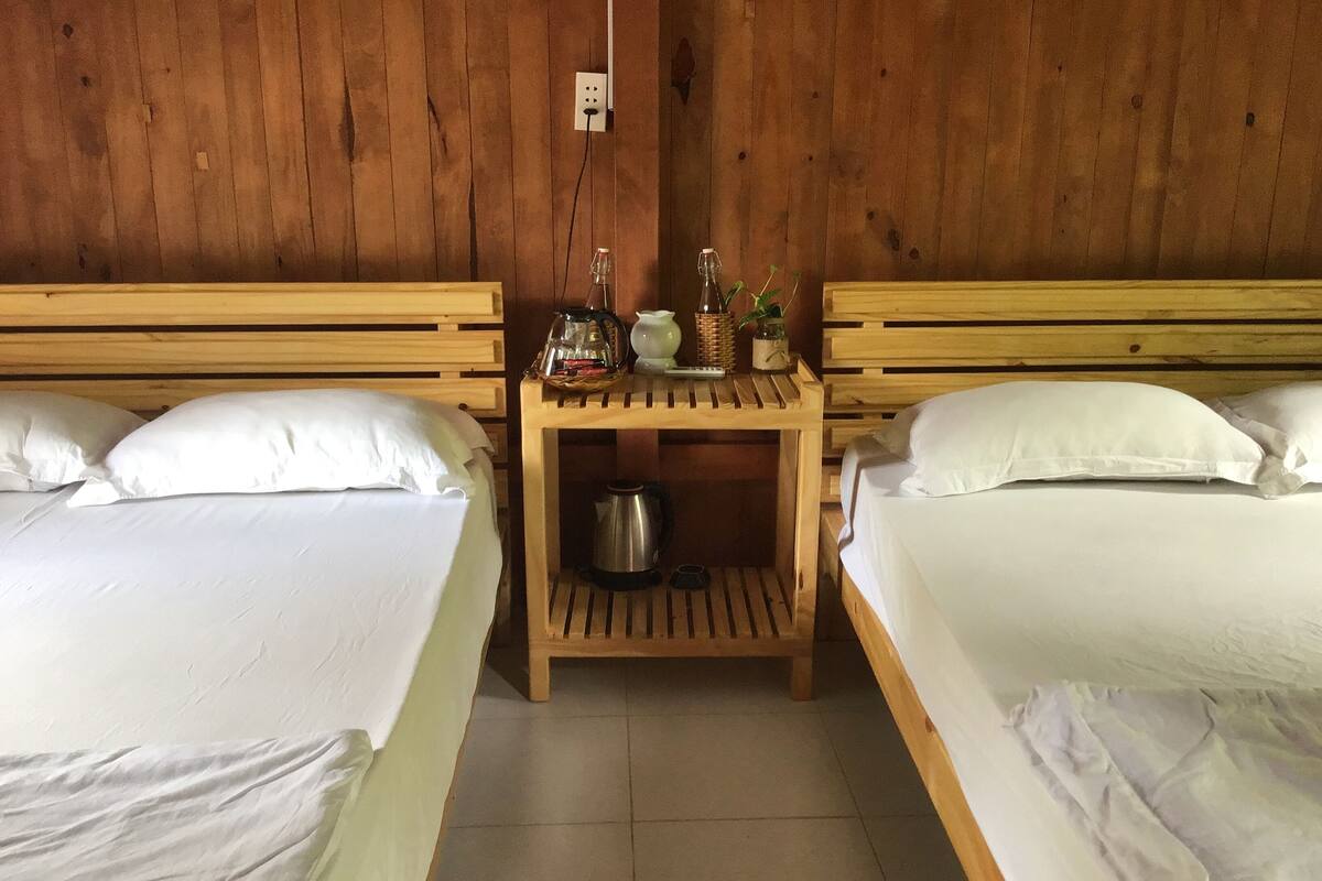 Una habitación con dos camas de madera, una mesita de noche de madera con un hervidor, y un enchufe de pared.