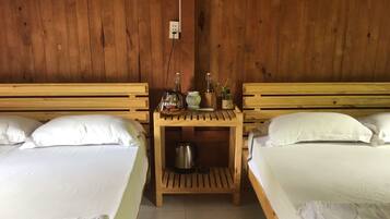 A room with two wooden beds, a small wooden nightstand with a kettle, and a wall socket.