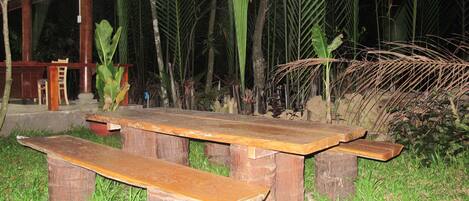 A wooden picnic table with benches, surrounded by lush greenery and palm trees.