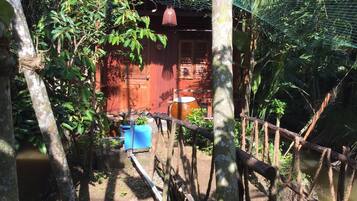 A rustic wooden house with a red door, surrounded by lush greenery and a wooden fence.