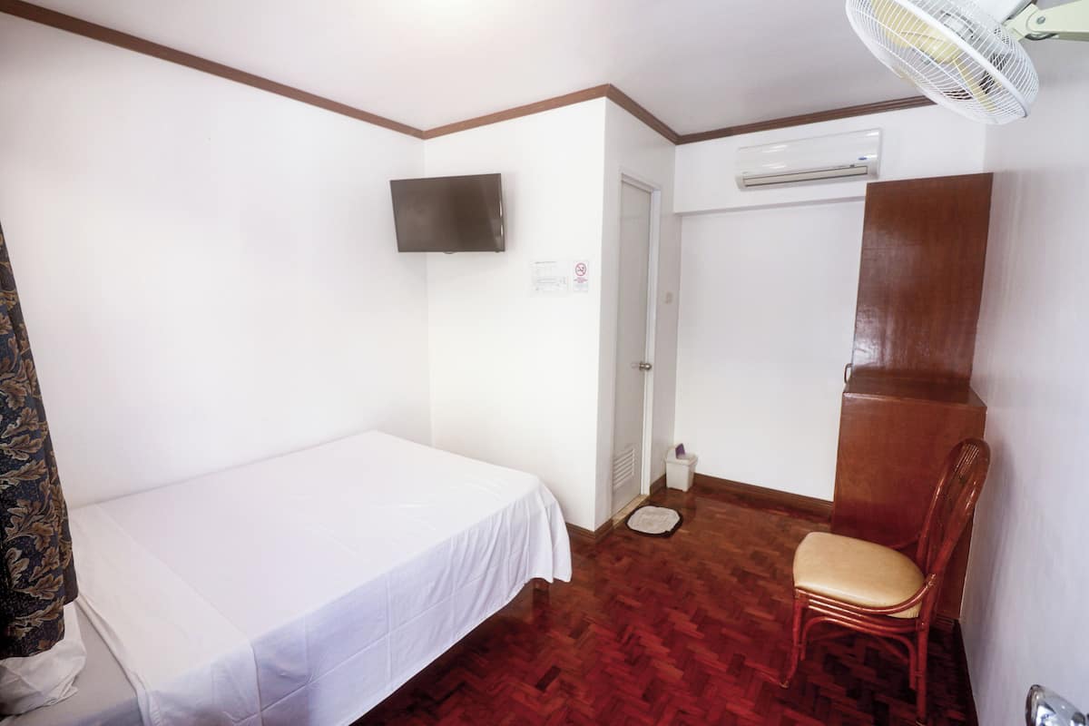 Une chambre comprenant un lit, une chaise, un téléviseur, un appareil de climatisation et un ventilateur.