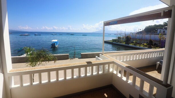 Un balcón con vista al mar, un pequeño jardín y una barandilla blanca.