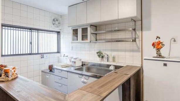 A modern kitchen with white cabinets, a wooden countertop, a stainless steel sink, and a window with blinds. - Funhouse Katsuragawa (Kyoto)