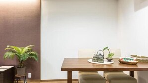 A dining area with a wooden table, two chairs, a potted plant, a teapot, and a small table with a bowl and a basket. - Funhouse Katsuragawa (Kyoto)