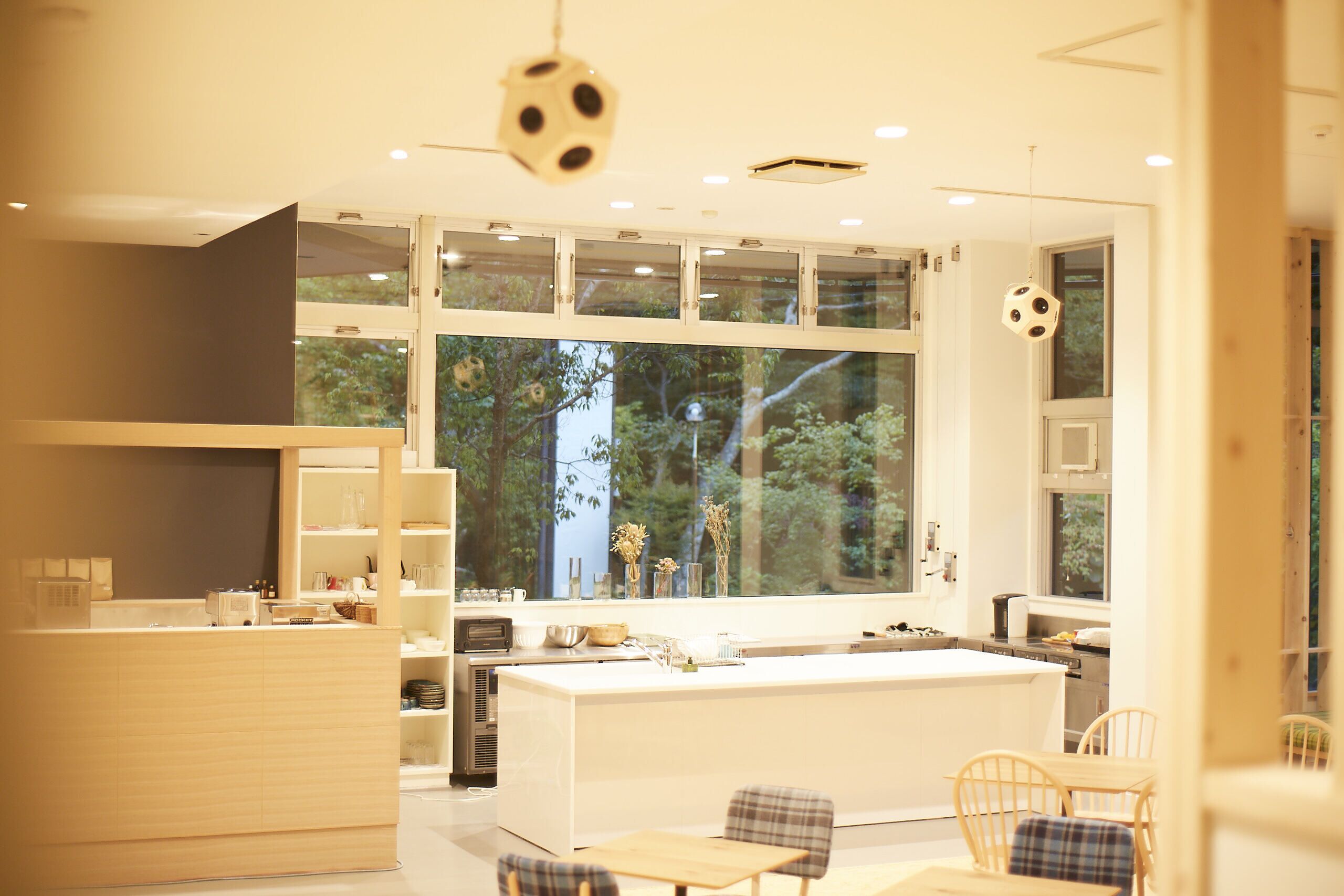 A modern kitchen with a large island, wooden chairs, and a view of greenery outside.