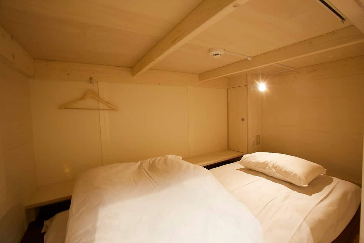 Ein kleines Zimmer mit einem Einzelbett, Holzboden und einem hängenden Kleiderhaken.