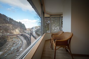 A balcony with a view of a river and a bridge, wicker chairs, and a tiled floor.