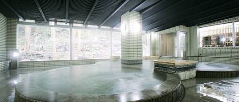 Un onsen japonés tradicional con una fuente termal circular, paredes de azulejos y ventanas amplias que permiten la entrada de luz natural.
