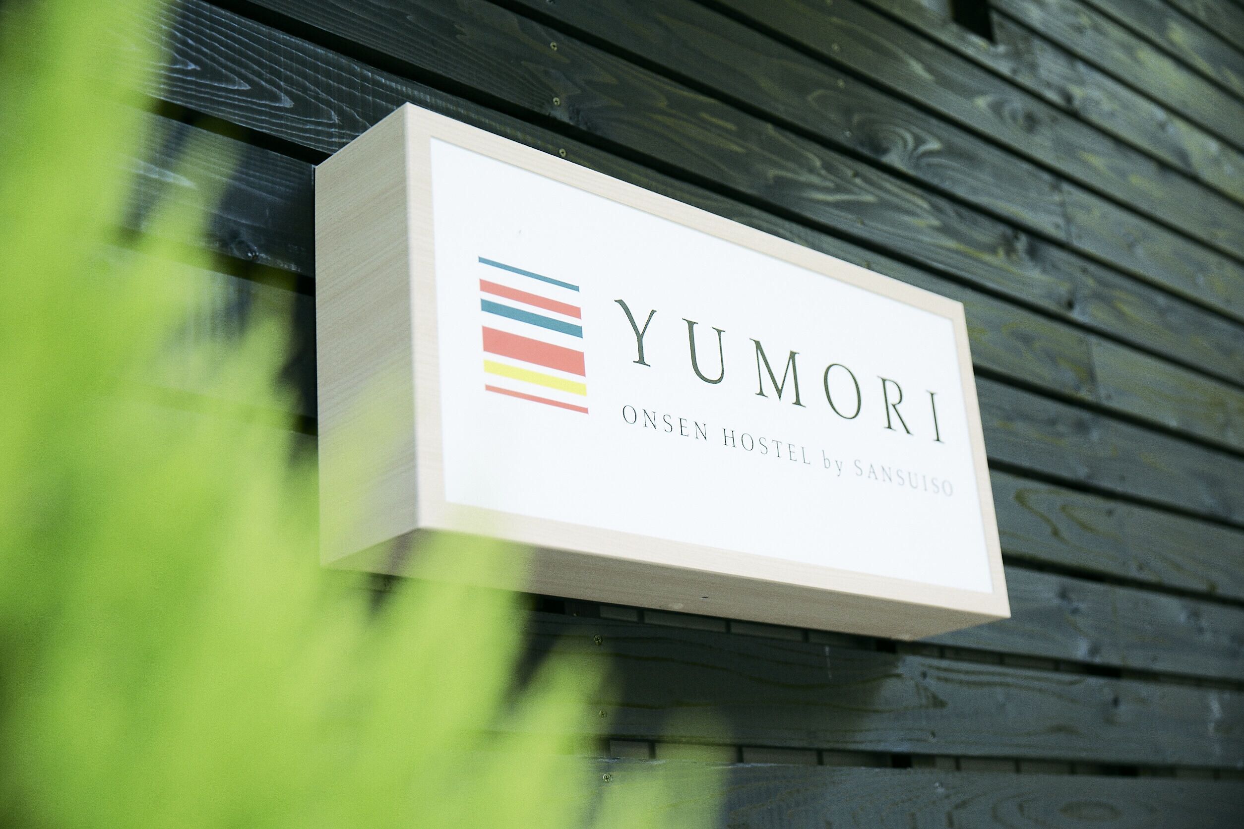 A sign for YUMORI, a hostel by Sansuiso, mounted on a wooden wall.