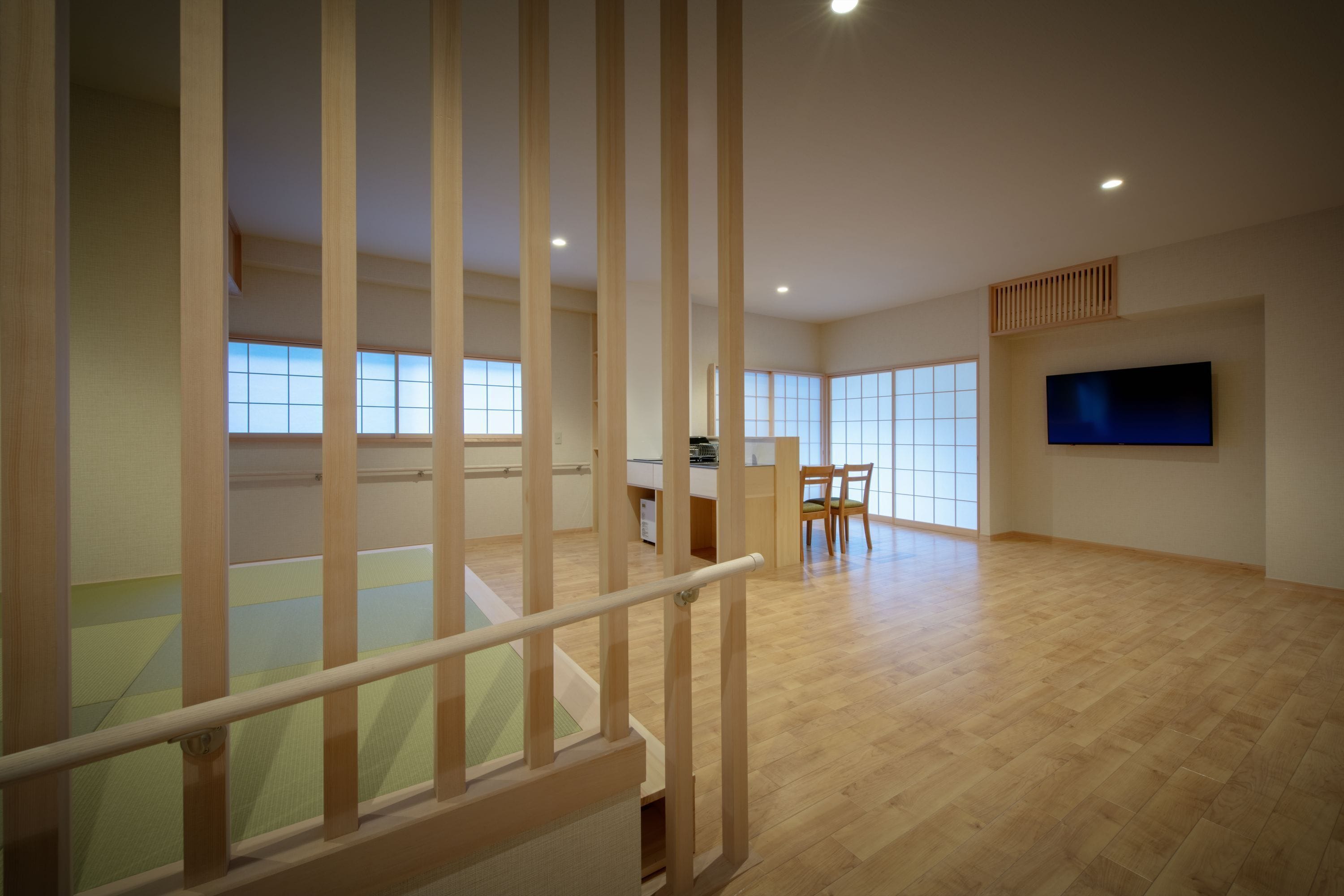 Amplia sala de estar con piso de madera, televisor montado en la pared y escalera con barandilla de madera.