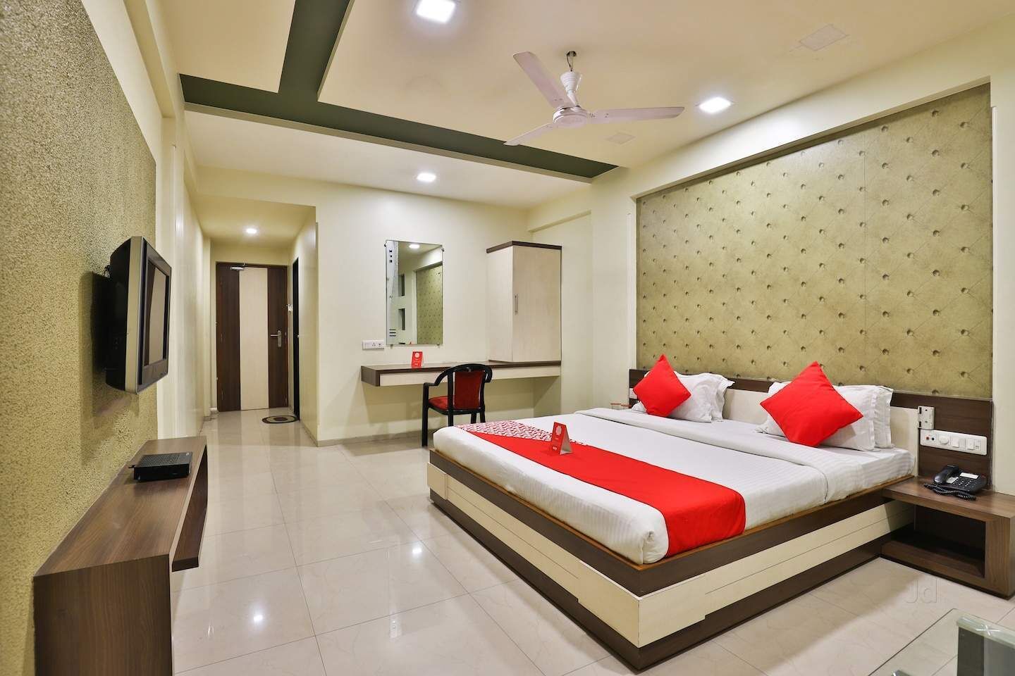 A hotel room with a bed, bedside table, nightstand, TV, desk, chair, and a mirror.