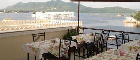 A terrace with tables and chairs, overlooking a body of water and a white building.