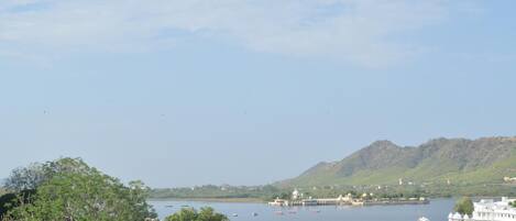 A calm lake with boats, a white building with domed structures, and a hill in the background.