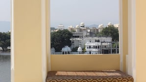 A balcony with a patterned floor, a decorative arch, and a view of buildings across a body of water. - Hotel Raj Niwas (Udaipur)