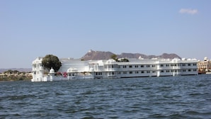 A large, white, multi-story building with domed roofs, situated by a body of water. - Hotel Raj Niwas (Udaipur)
