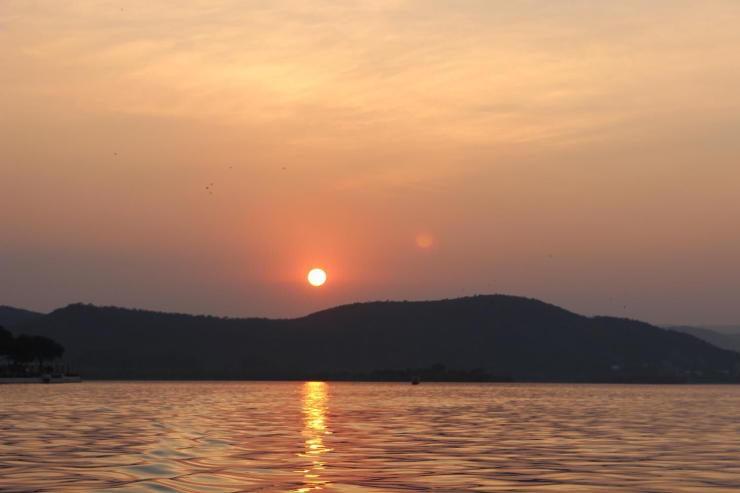 A sunset over a body of water with hills in the background.