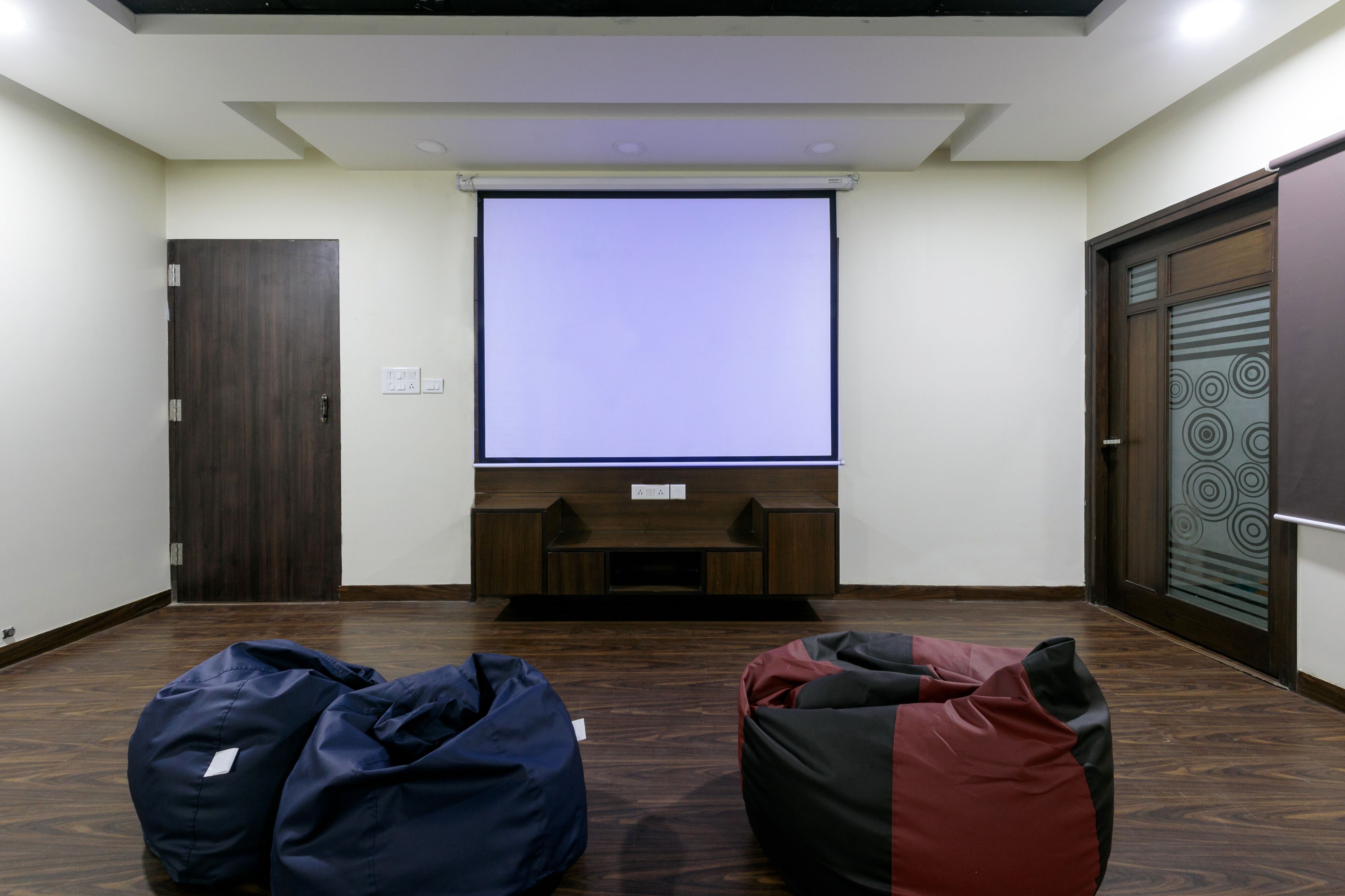 Una habitación con pantalla de proyector, suelo de madera y dos sillones tipo alcolchón.