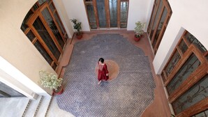 A spacious courtyard with a patterned floor, potted plants, and wooden-framed windows.