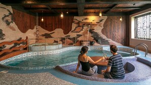 A couple sitting by a small indoor pool with mosaic tiles and wooden accents.