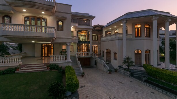 A large, multi-story building with a grand entrance, multiple balconies, and a well-maintained garden.