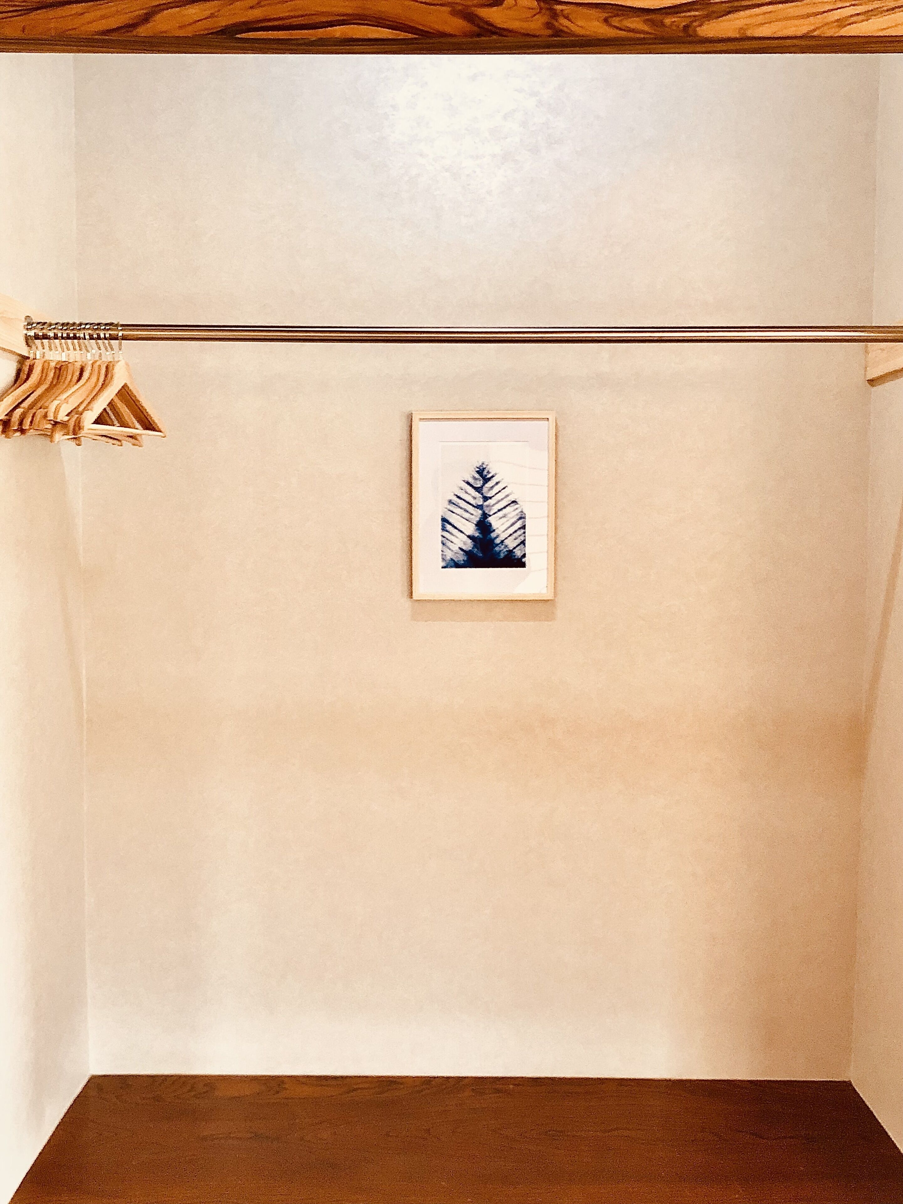Une pièce avec un plancher en bois, une œuvre d’art encadrée accrochée au mur et une tringle à rideaux sur laquelle est suspendu un rideau en bois.