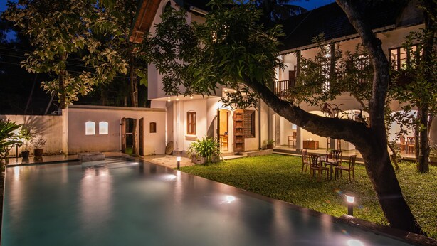 A poolside area with a clear view of the pool, a dining area with chairs, and a building with a door and windows.