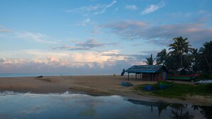 A beach with a small hut and boats, palm trees, and a calm sea.