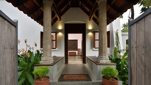 A covered entrance with a wooden roof, two potted plants, and a pathway leading to a room.