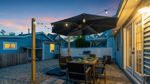 An outdoor patio with a table set for dining, surrounded by chairs and a large umbrella.