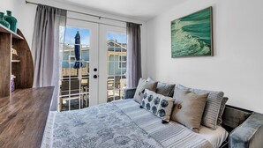 A bedroom with a large bed, a wooden nightstand, a view of the outside through a sliding glass door, and a painting on the wall.
