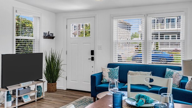 A living room with a blue sofa, a flat-screen TV, and a large window with blinds.